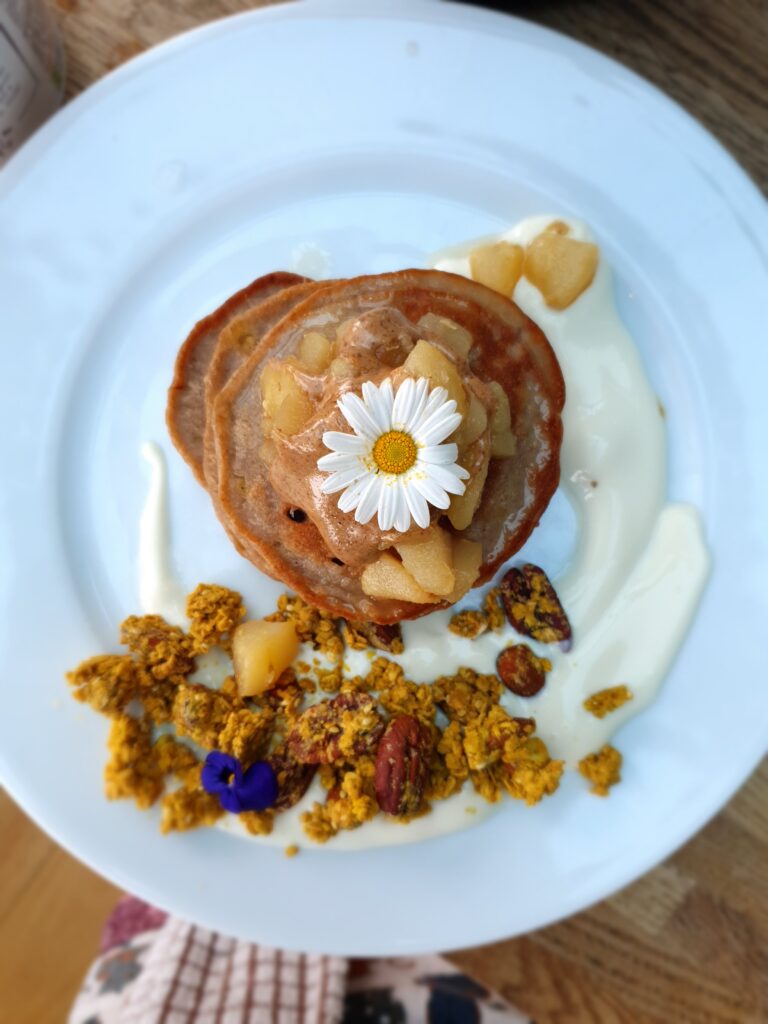 buckwheat banana pancakes with chunky turmeric granola, almond butter and decorated with an edible flower and yoghurt